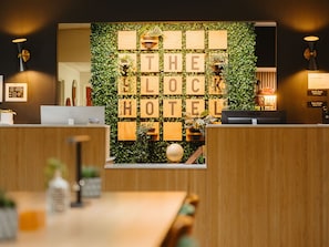 Ein Empfangsbereich mit einem Holztisch, einem Computer und einer Wand mit Holzwürfeln, die 'THE BLOCK HOTEL' buchstabieren.