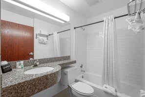 Un baño con encimera de granito, inodoro, bañera y cortina de ducha.