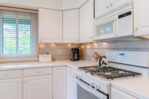 A kitchen with white cabinets, a stove, a microwave, and a coffee maker. - Charming 1-bedroom Downtown Escape in Saugatuck, perfect for solo travelers. (Saugatuck)