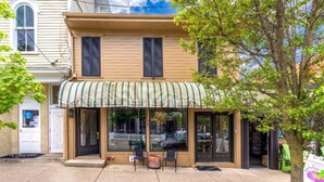 A two-story building with a storefront featuring a striped awning and large windows. - Charming 1-bedroom Downtown Escape in Saugatuck, perfect for solo travelers. (Saugatuck)