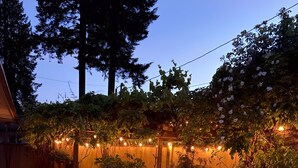A hot tub with a tiled edge, surrounded by a brick patio, and string lights in the background. - Casa Capilano (North Vancouver)