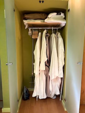 Ein begehbarer Kleiderschrank mit hängender Kleidung, einem Regal mit gefalteten Gegenständen und einem Staubsauger auf dem Boden.