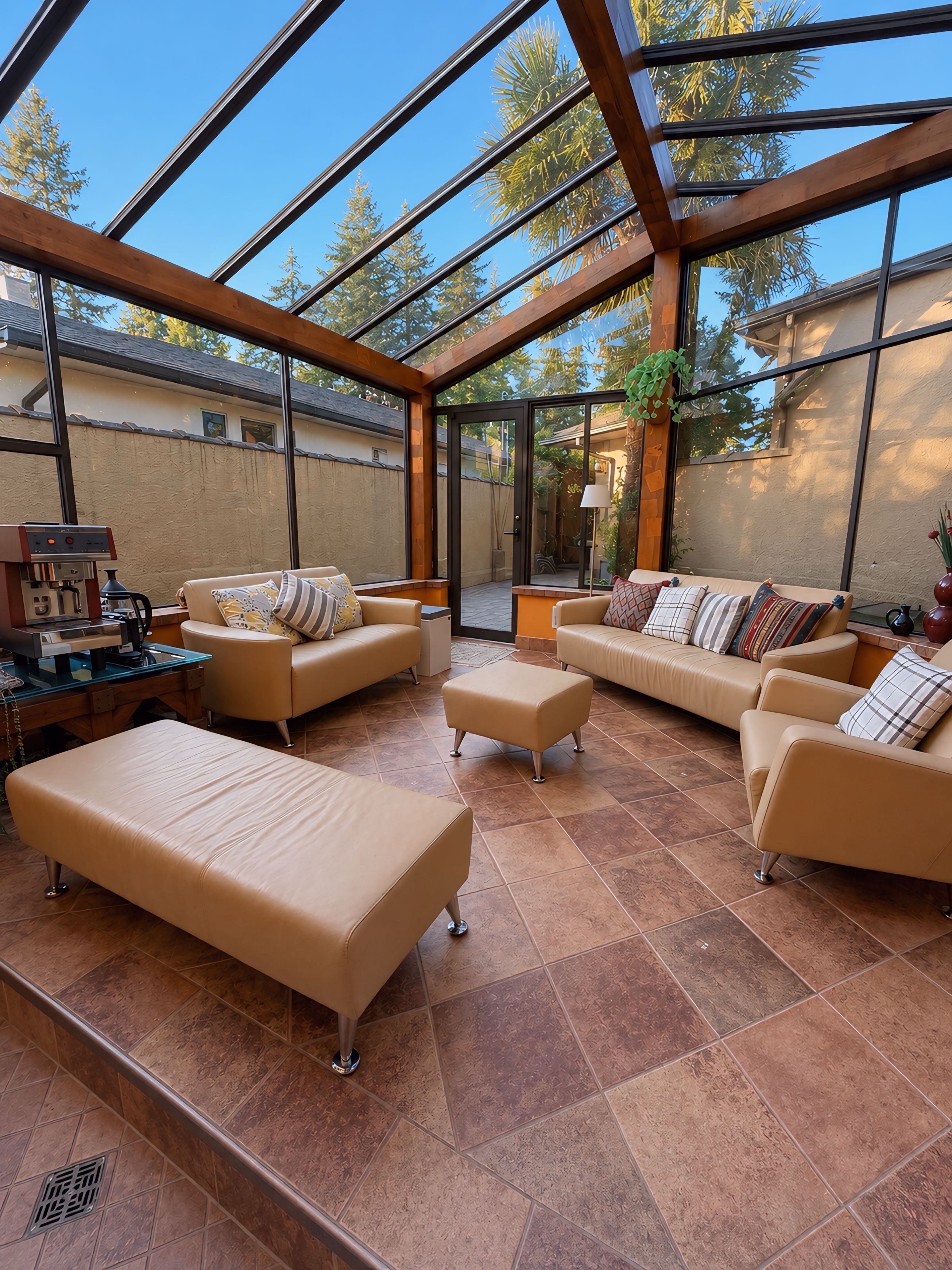 A sunlit room with a glass ceiling, beige sofas, a coffee station, and a view of trees.