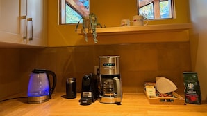 A kitchen with a coffee maker, kettle, and coffee beans. There are two windows with a view of the outside. - Casa Capilano (North Vancouver)