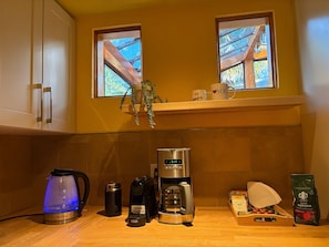 Eine Küche mit Kaffeemaschine, Wasserkocher und Kaffeebohnen. Zwei Fenster bieten einen Blick ins Freie.