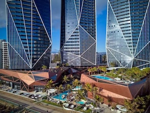Un complexe hôtelier moderne composé de plusieurs immeubles de grande hauteur, doté d’une piscine sur le toit et agrémenté de palmiers.