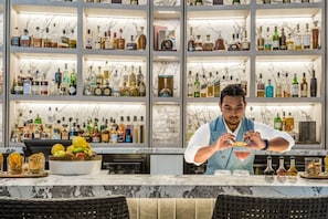 A bar area with shelves of liquor bottles, a bartender preparing a drink, and a bowl of fruit on the counter. - Champagne Oceanview Suite- The Langham- wParking (Surfers Paradise)
