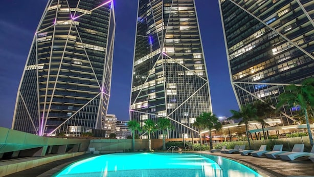 Um hotel moderno com piscina, arranha-céus e palmeiras.