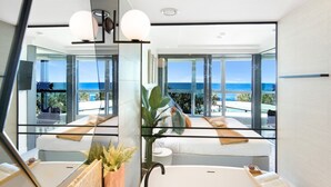 Uma casa de banho moderna com um espelho grande, uma banheira e vista para o oceano.