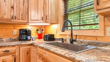 A kitchen with wooden cabinets, a granite countertop, a coffee maker, a toaster, and a window with blinds.