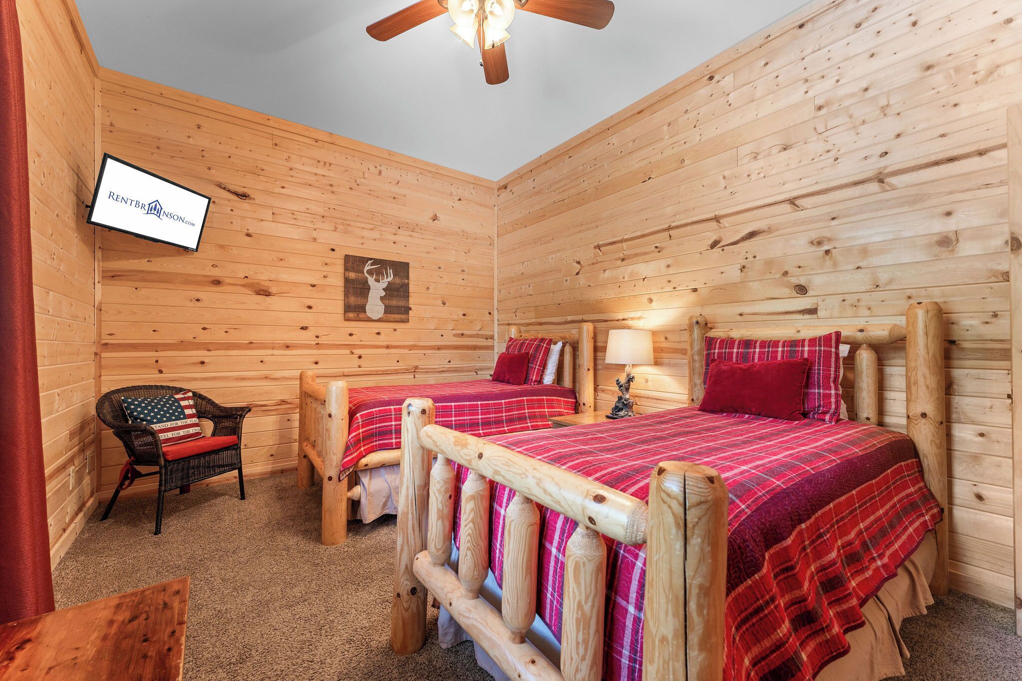 A wooden cabin room with two beds, a television, and a chair.
