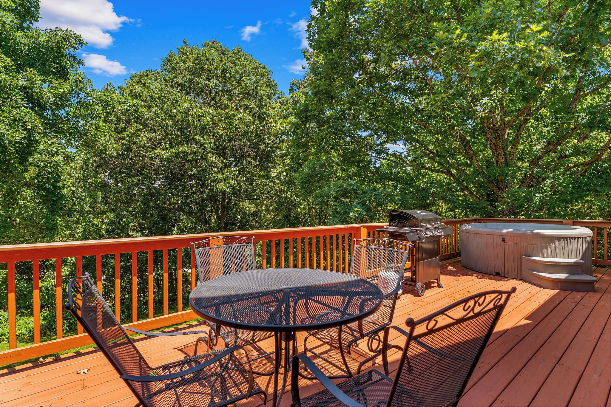 A deck with a round table and chairs, a hot tub, and a grill.