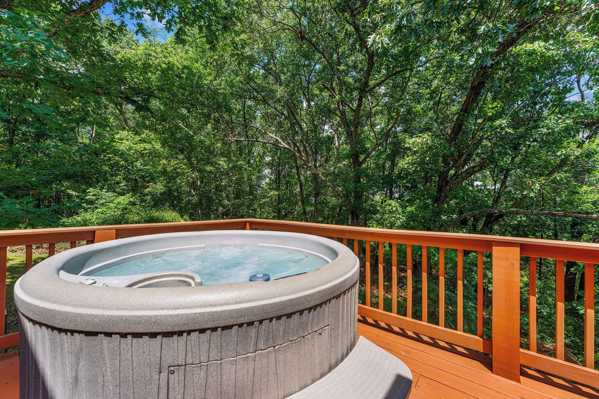 A hot tub on a wooden deck surrounded by lush green trees.