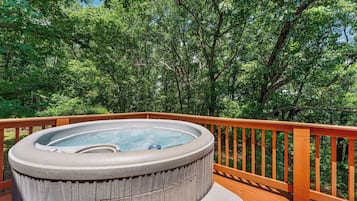 A hot tub on a wooden deck surrounded by lush green trees.