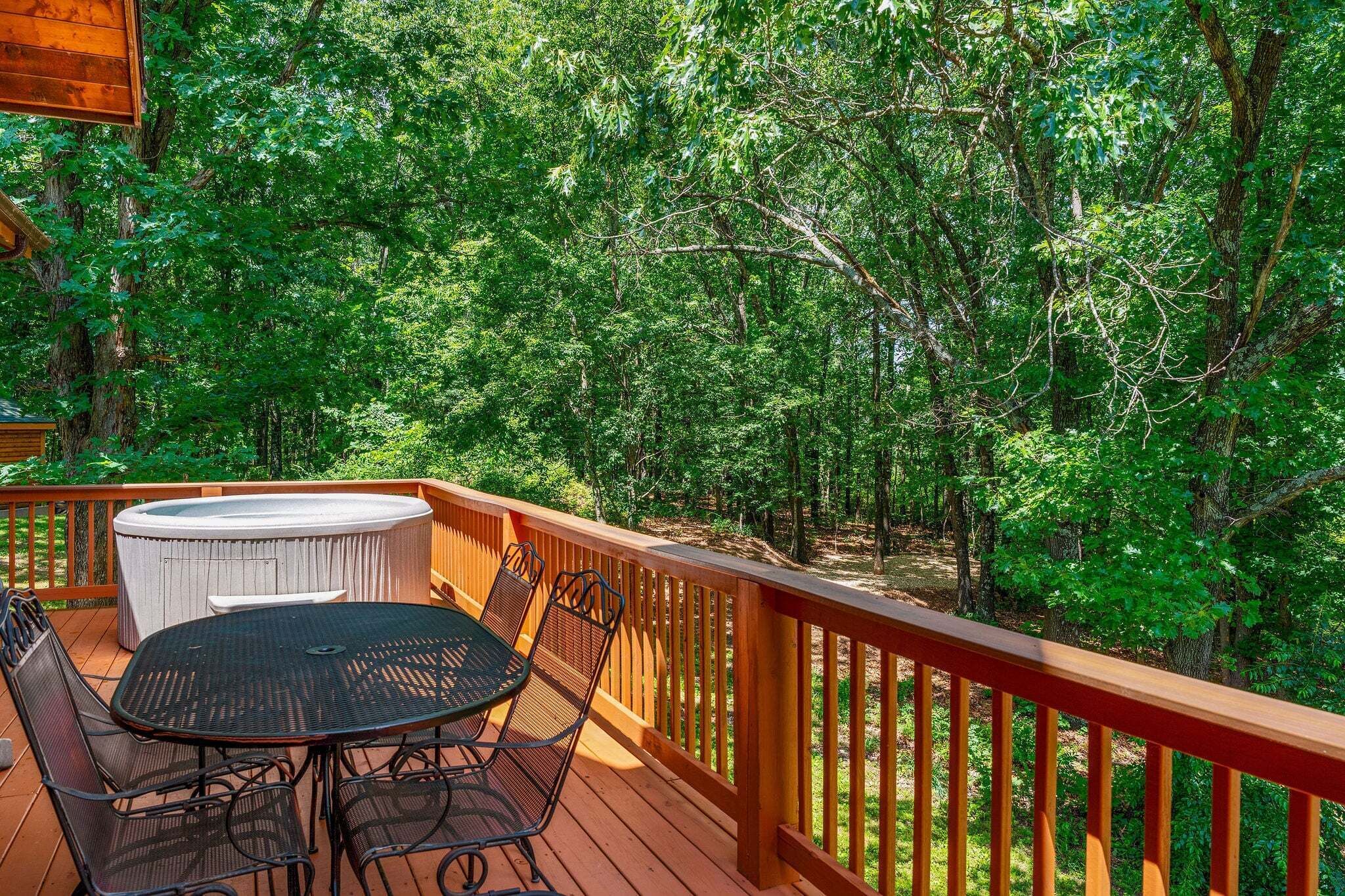 Une terrasse en bois avec un jacuzzi, une table et des chaises, le tout entouré d’une forêt dense.