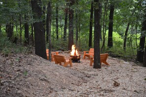 A campsite with a fire pit surrounded by wooden chairs and benches. - Secluded Ozark Log Cabin w/ Private Fire Pit, Hot Tub & Pool Table (Ridgedale)