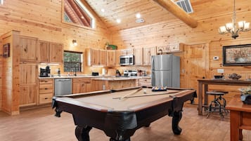 A wooden interior with a pool table, kitchen area, and a dining table with stools.