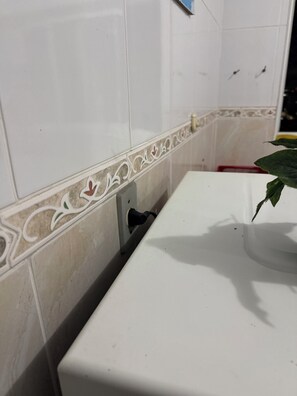 A bathroom with white tiles, a sink, and a decorative border. - Pé na Areia Praia da Guilhermina VII (Praia Grande)