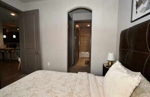 Une chambre à coucher avec un lit, une table de chevet avec une lampe et une porte en arc donnant sur une salle de bain.