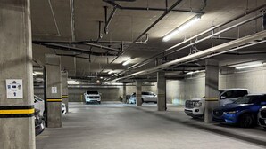 Un estacionamiento subterráneo de varios niveles con pilares de hormigón, tuberías y luces fluorescentes.