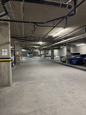 A multi-level underground parking garage with concrete pillars, overhead pipes, and fluorescent lighting. - Our Home Your Holiday (Canmore)