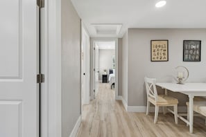 Ein Flur mit einer weißen Tür, einem weißen Tisch mit einem Stuhl und zwei gerahmten Bildern an der Wand.