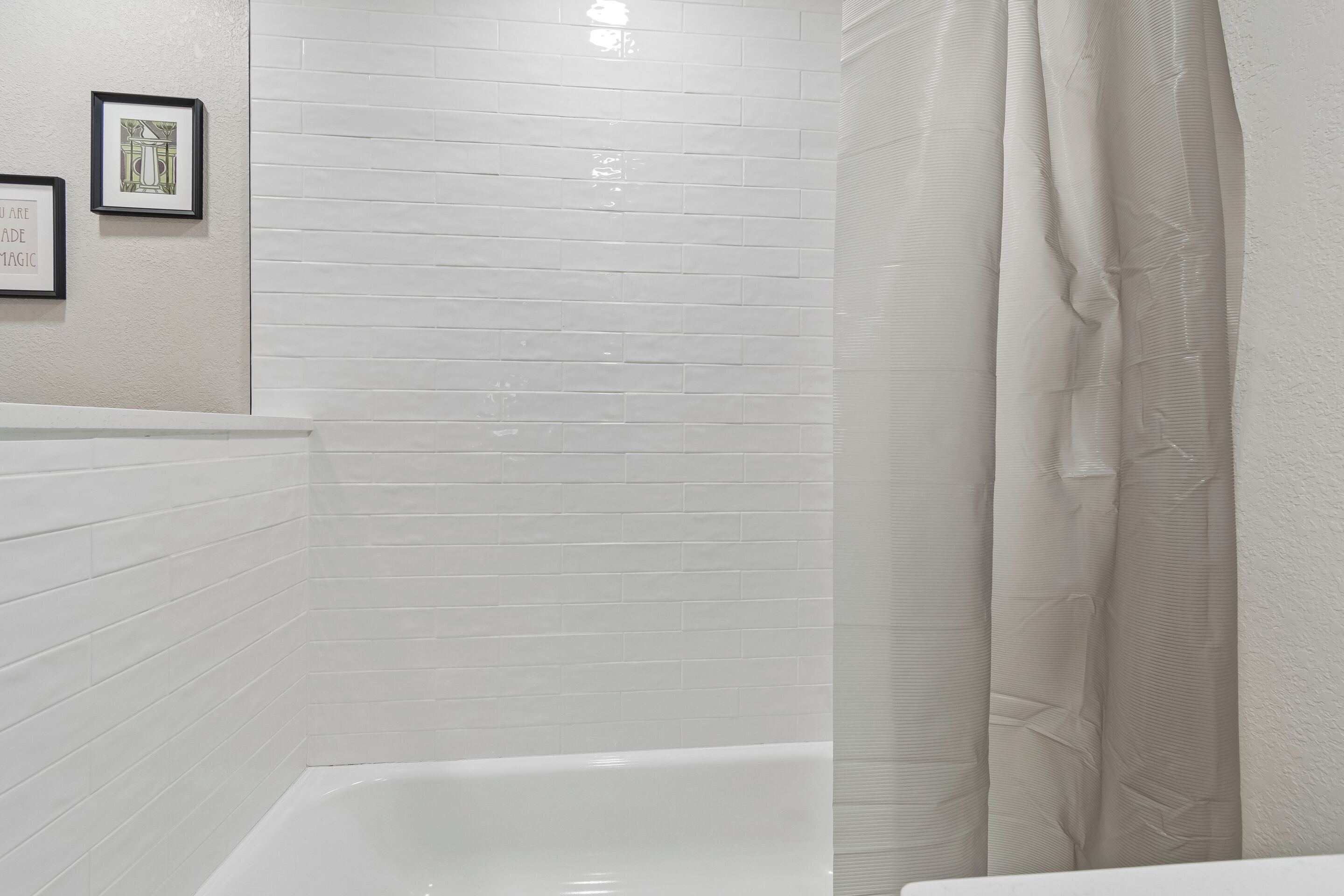 Un baño con paredes de azulejos blancos, una bañera blanca y una cortina de ducha.