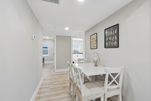 A dining area with a white table and chairs, a window with blinds, and a framed picture on the wall.