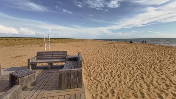 Een strand met een houten terras en een duinpaal.