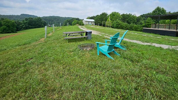 A grassy outdoor area with picnic tables, a fire pit, and a blue chair.