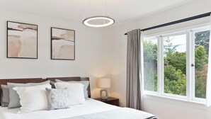 Un dormitorio con una cama, dos cuadros abstractos colgados en la pared, una lámpara de noche y una ventana con cortinas.