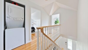 Una sala de lavandería con lavadora y secadora, una escalera con balaustres blancos y una planta al fondo.