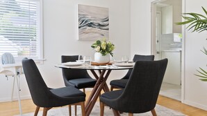 Un comedor con una mesa redonda, cuatro sillas, un jarrón con flores y un cuadro en la pared.