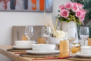 Ein Esstisch ist gedeckt mit weißen Schüsseln, Tassen mit goldener Kante und klaren Gläsern, dazu steht eine Vase mit rosa Rosen und weißen Blumen.