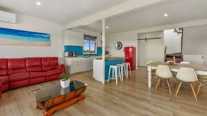 A modern living room with a red sofa, a glass coffee table, and a kitchen area with a blue island and white stools. - Get away at Rivoli Bay Farm Stay. Beach access close by. Sleeps 6 (Beachport)