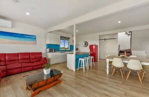 Ein modernes Wohnzimmer mit einem roten Sofa, einem Glastisch und einer Küchenzeile mit einer blauen Kochinsel und weißen Barhocker.