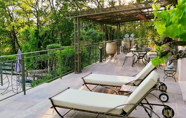 An outdoor patio with two lounge chairs, a pergola, a table with chairs, and a large urn. - Lovely home in Lorgues (Lorgues)