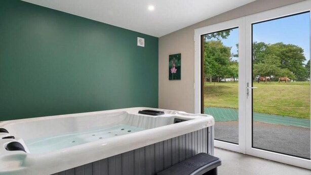 Ein Wellnessraum mit Whirlpool, einer Bank und einer Schiebetür zu einem grünen Außenbereich.