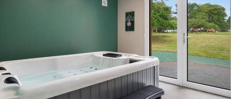 A spa room with a hot tub, a bench, and a sliding glass door leading to a grassy outdoor area.