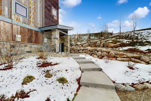 A building with a stone facade, a stone staircase leading to a door, and a snow-covered landscape. - Mountain view condo w/ shared pool, hot tub, gym (Keystone)