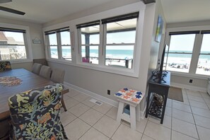 Ein Zimmer mit Esstisch, Stühlen, einem kleinen Tisch mit Spielzeug und großen Fenstern mit Blick auf den Strand.