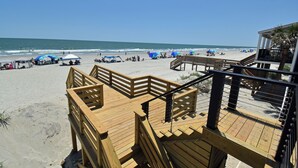 A wooden deck with a railing, leading to a beach area with umbrellas and beach chairs. - Krazy Krab - Oceanfront in Garden City Beach (Garden City)