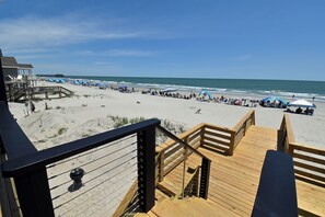 Blick auf einen Strand mit einer Holzterrasse, Strandzelten und einem Pier im Hintergrund.