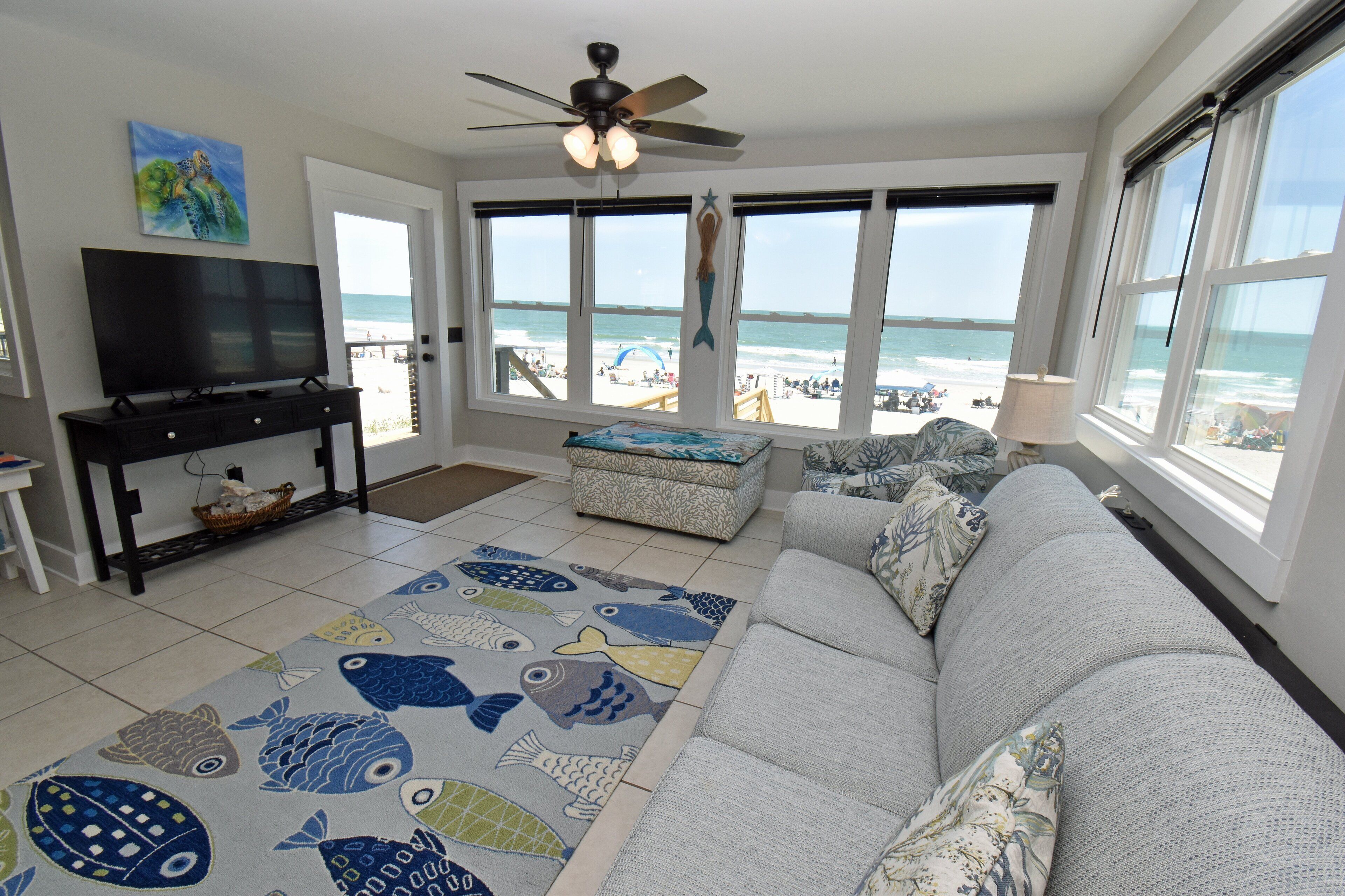 A living room with a large window, a ceiling fan, a flat-screen TV, and a patterned rug.