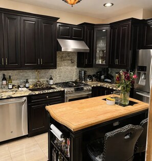 Una cocina con armarios oscuros, electrodomésticos de acero inoxidable, una isla de madera y un florero con flores.