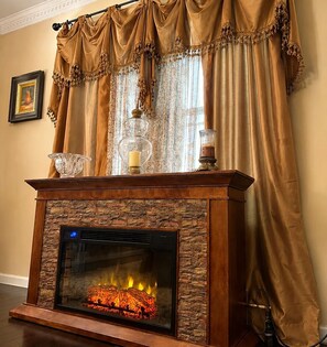 Una chimenea con fachada de piedra, un repisa con adornos y cortinas con flecos.