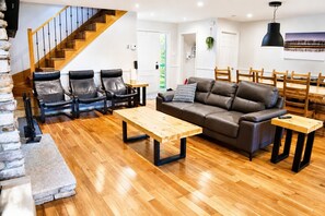 Ein modernes Wohnzimmer mit einer Holztreppe, Ledersofas, einem Holztisch und einem Essbereich mit Holzsesseln.