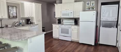 A modern kitchen with white cabinetry, a granite countertop, a built-in oven, a microwave, and a refrigerator.