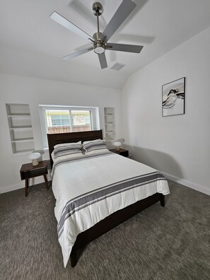 A bedroom with a bed, a ceiling fan, a window with blinds, a bedside table with a lamp, and a wall-mounted artwork. - Songbird Luxury Retreat — a Modern 4BR Getaway in Wylie, Near Lake Lavon (Wylie)