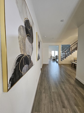 A hallway with wooden flooring, a staircase with metal railings, and abstract wall art. - Songbird Luxury Retreat — a Modern 4BR Getaway in Wylie, Near Lake Lavon (Wylie)